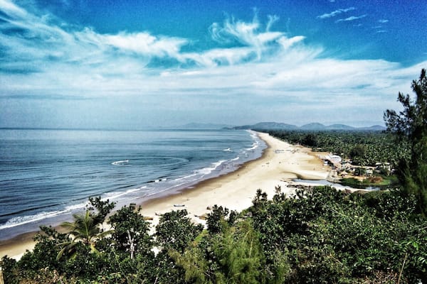 A beach with clear blue water, sandy shore, and lush greenery.