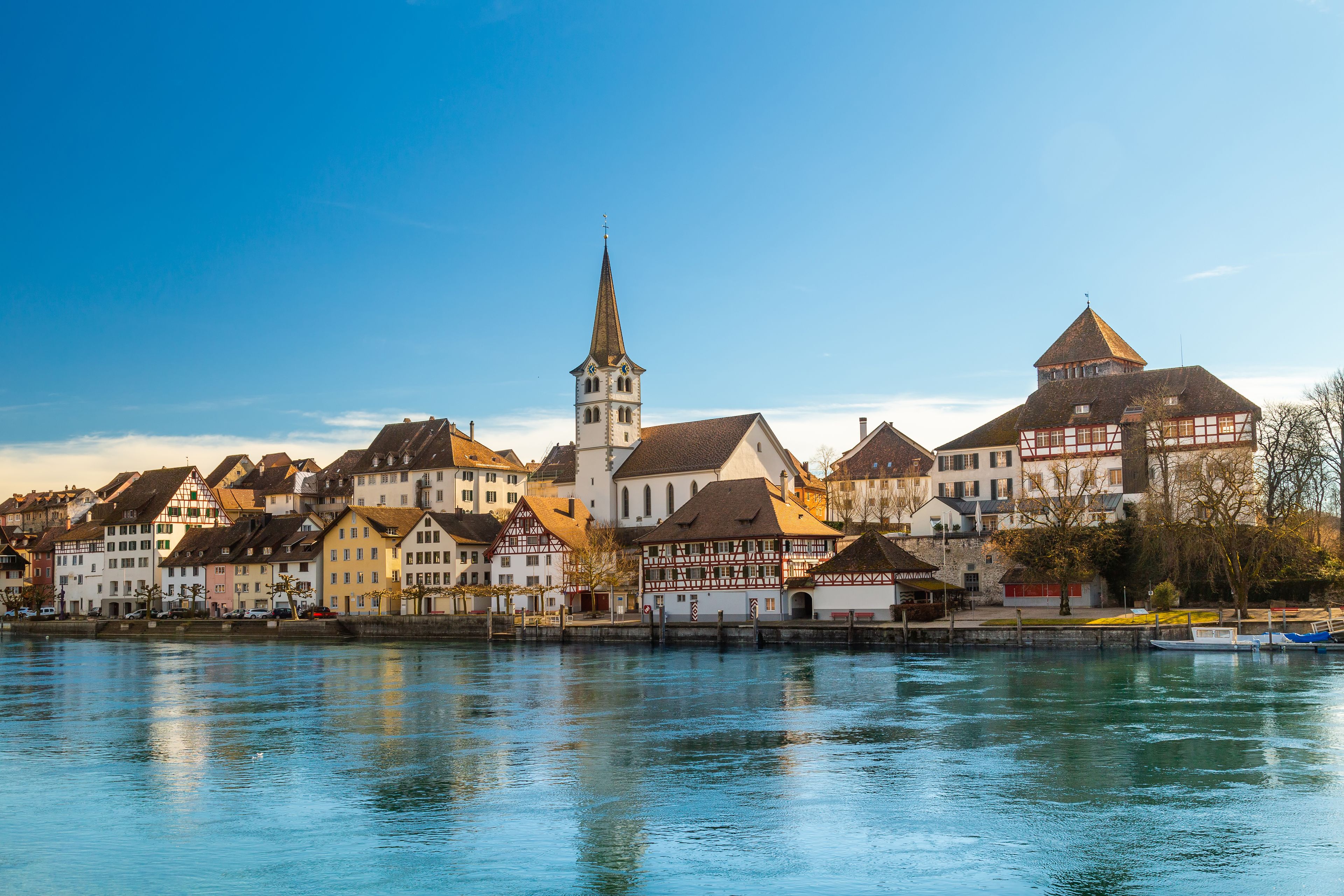 A riverside town with historic buildings, a church tower, and a clear blue sky.