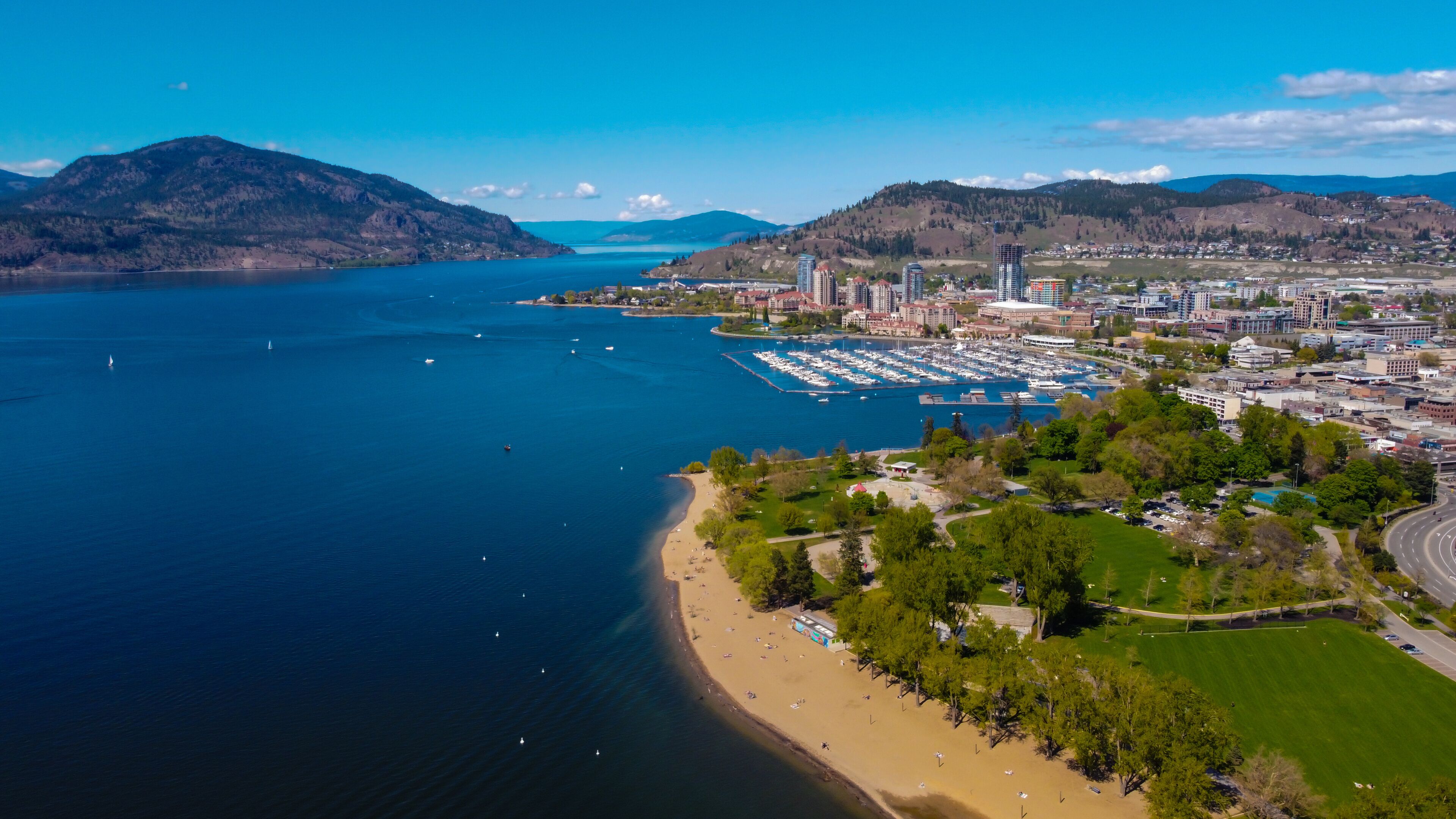A coastal city with a marina, sandy beach, and mountains in the background.