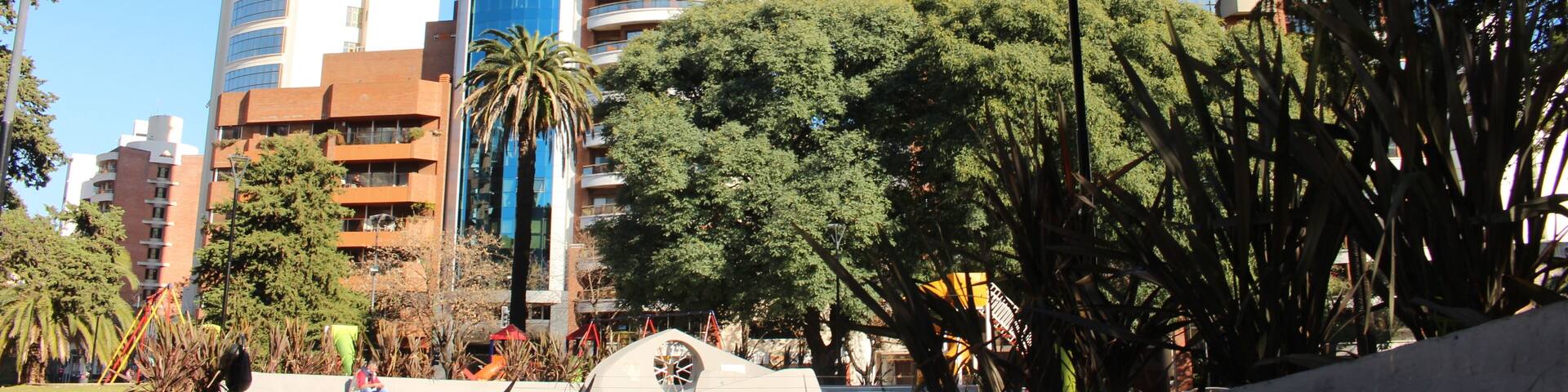 Un paisaje urbano con edificios modernos, una palmera y un parque infantil.