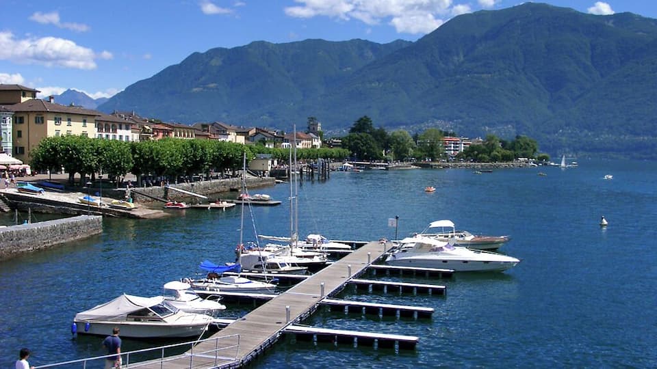 A marina with boats docked, a pier, and mountains in the background.