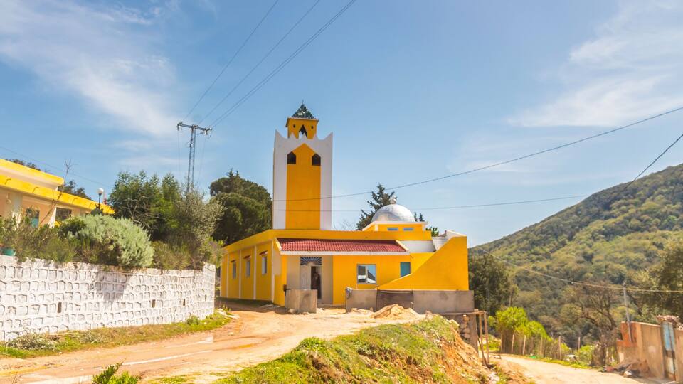A yellow church with a bell tower and a stone wall.