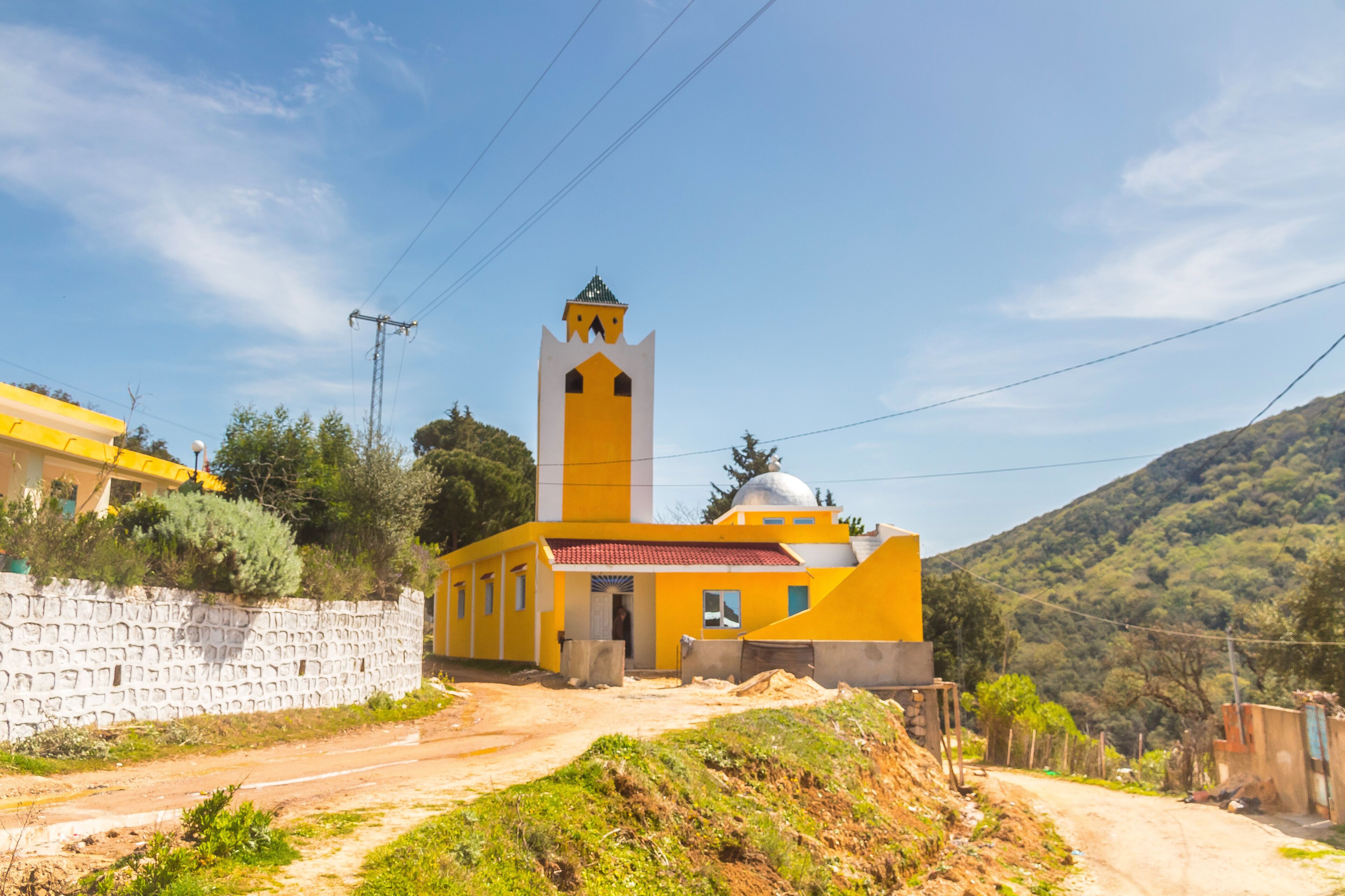 A yellow church with a bell tower and a stone wall.