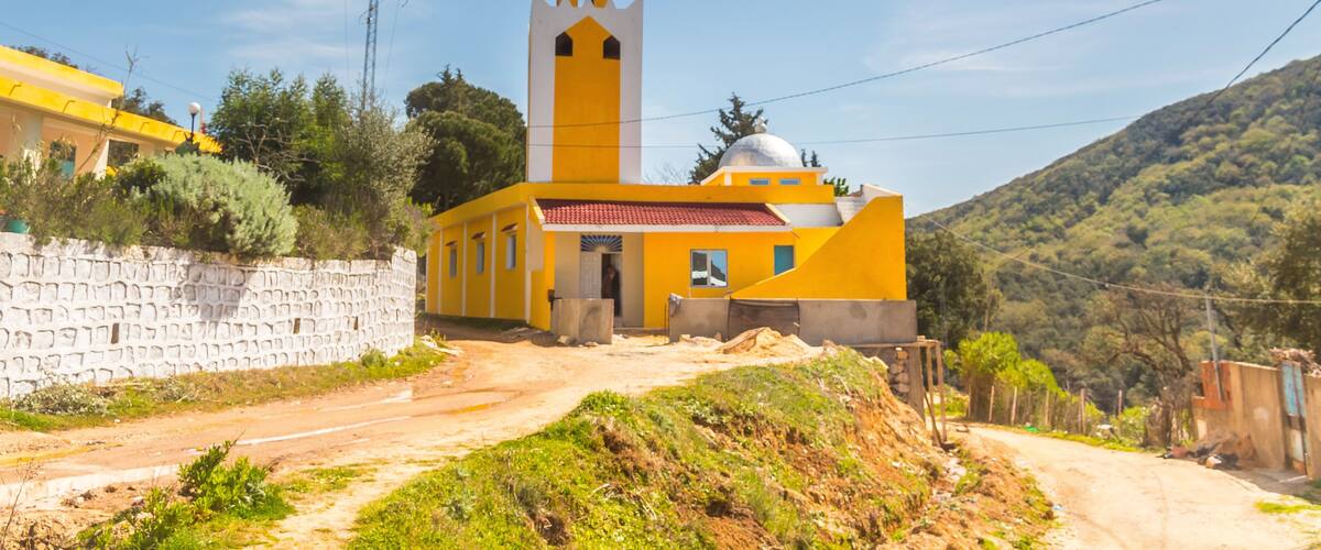 A yellow church with a bell tower and a stone wall.