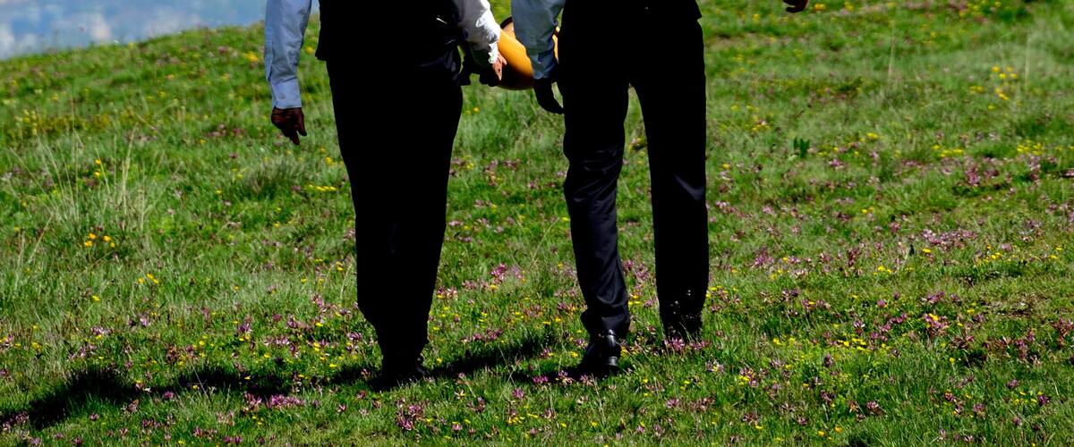 Nendaz, Conthey District,
Valais, Wallis, Switzerland, Europe - two men in traditional black vests, trousers and hats walking with alphorn on their arms, Swiss Alps, Nendaz village seen in valley