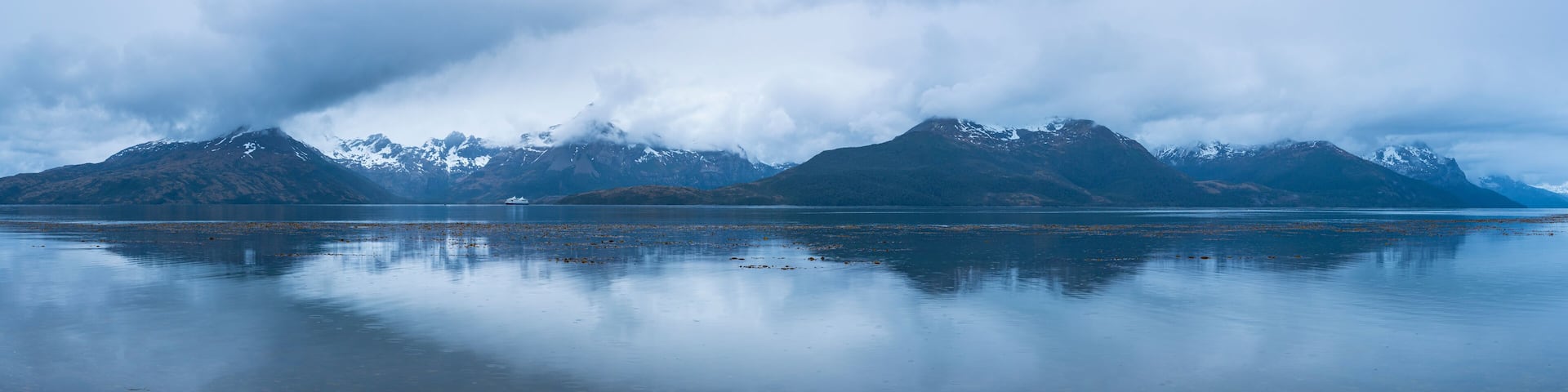A calm lake with mountains in the background and a boat in the water.