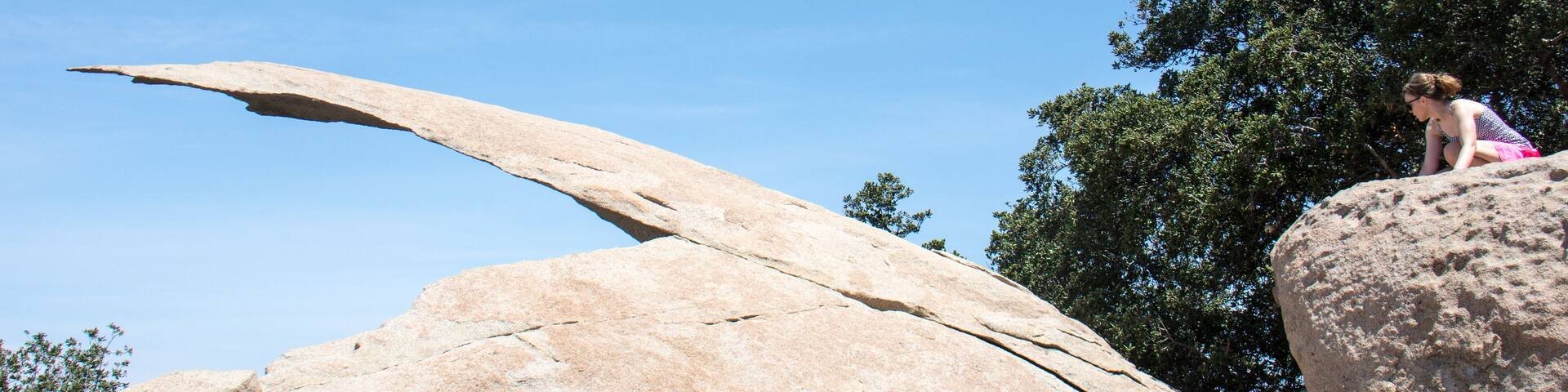 Young adult woman hiker attempts to get on top of Potato Chip Rock in Ramona California in San Diego