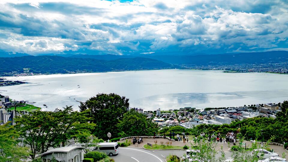 A coastal cityscape with a large body of water, a curved road, and a dense green park area.