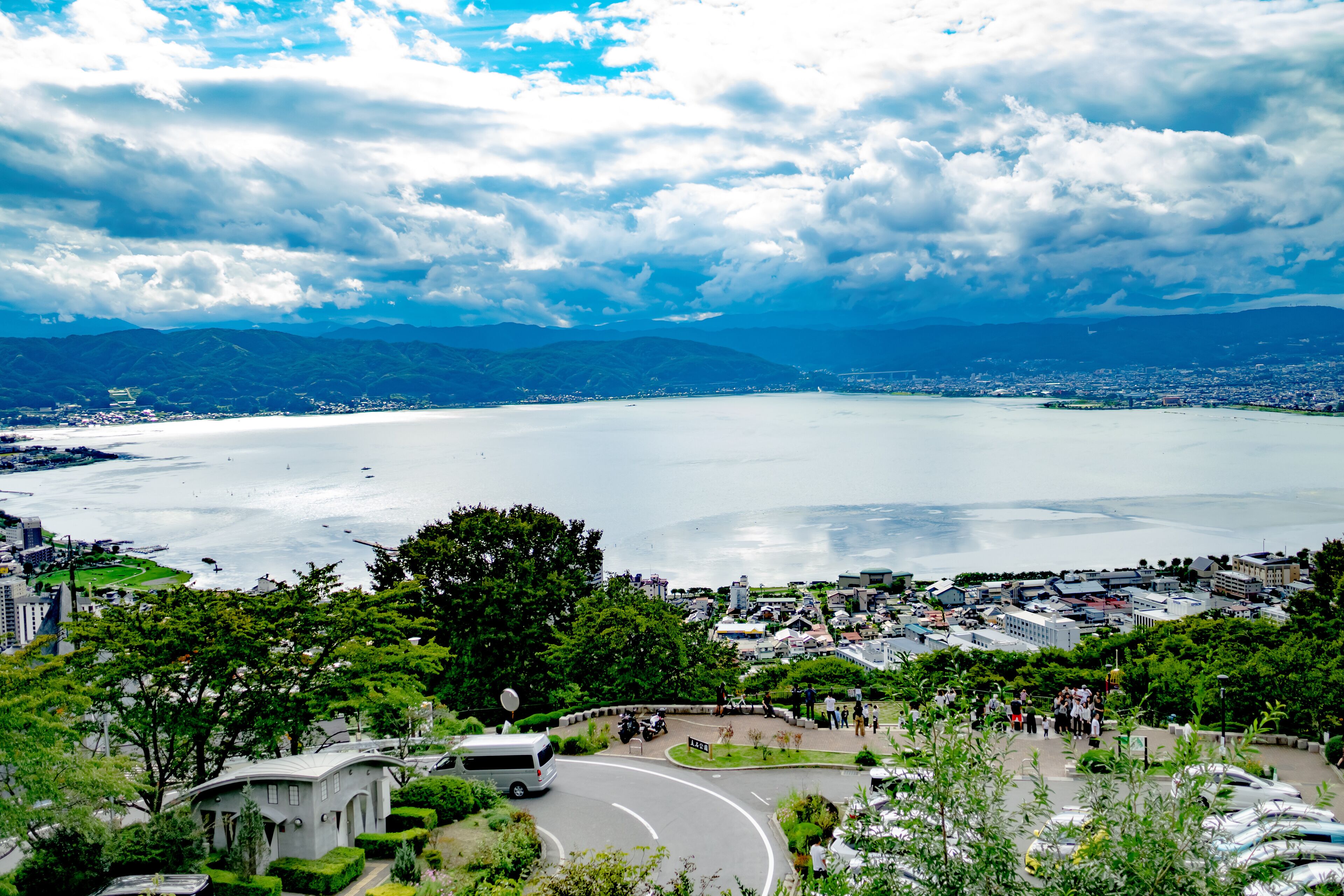 A coastal cityscape with a large body of water, a curved road, and a dense green park area.