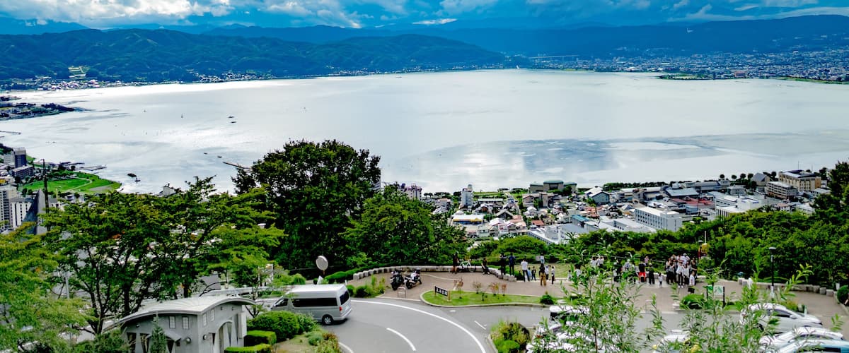 A coastal cityscape with a large body of water, a curved road, and a dense green park area.