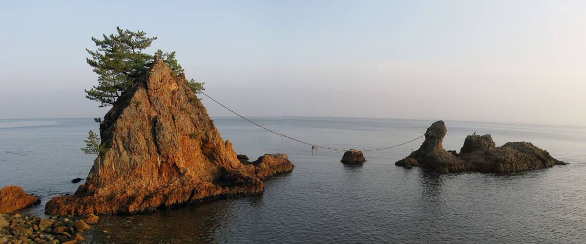 A rocky coastline with a rope bridge connecting two cliffs over calm water.