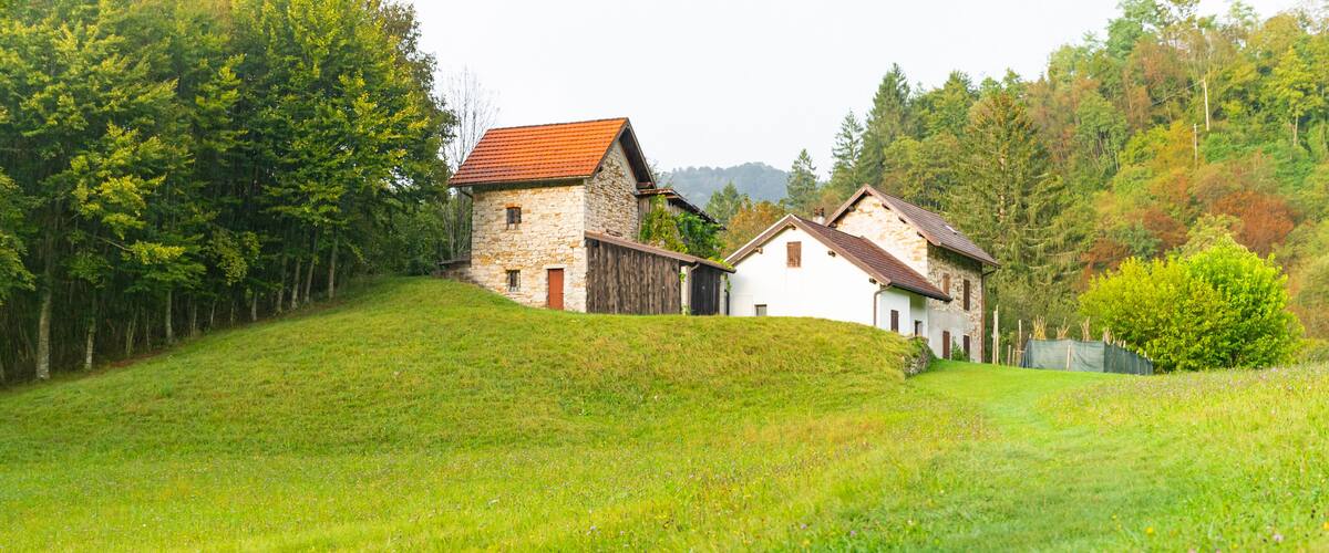 A rural landscape with a stone house and a white house on a grassy hill.