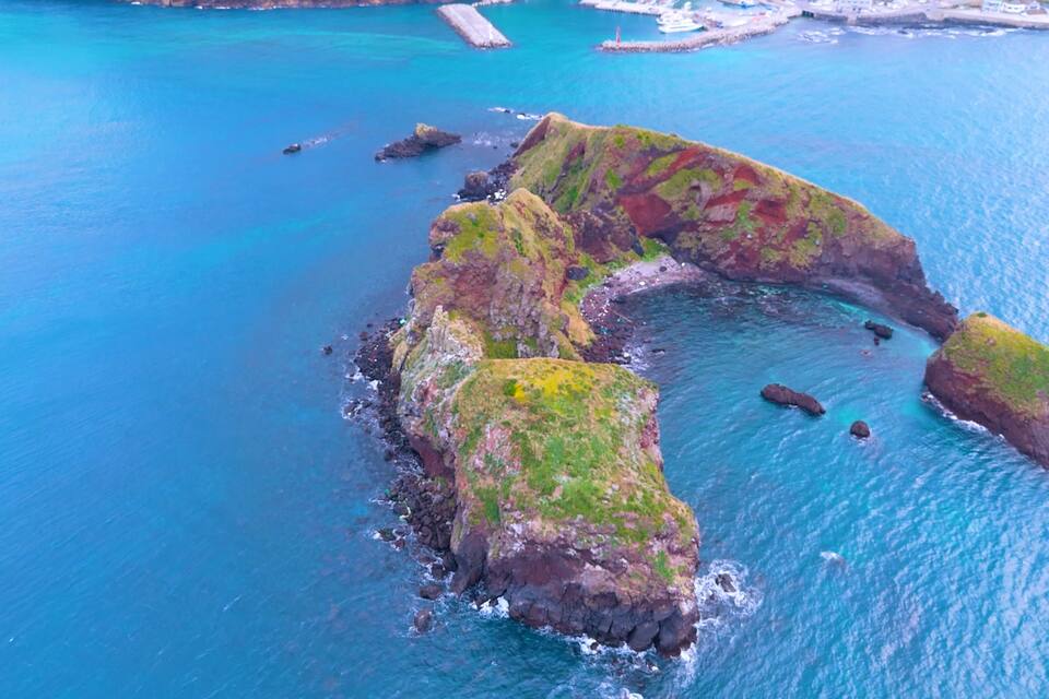 Paesaggio costiero con una roccia prominente a forma di arco sopra il mare turchese.