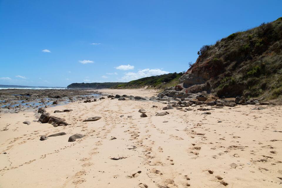 A sandy beach with scattered rocks and a rocky cliff.