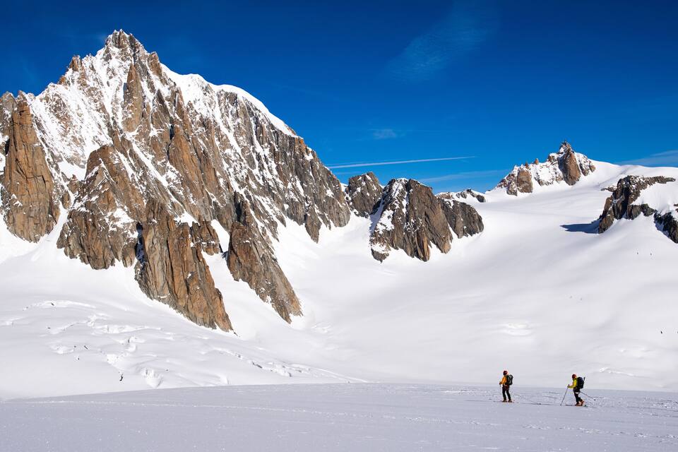 A snow-covered mountain range with two skiers.