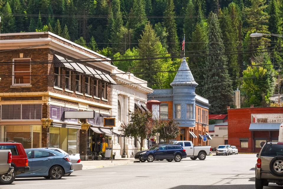 A street with historic buildings, a clock tower, and cars parked along the road.