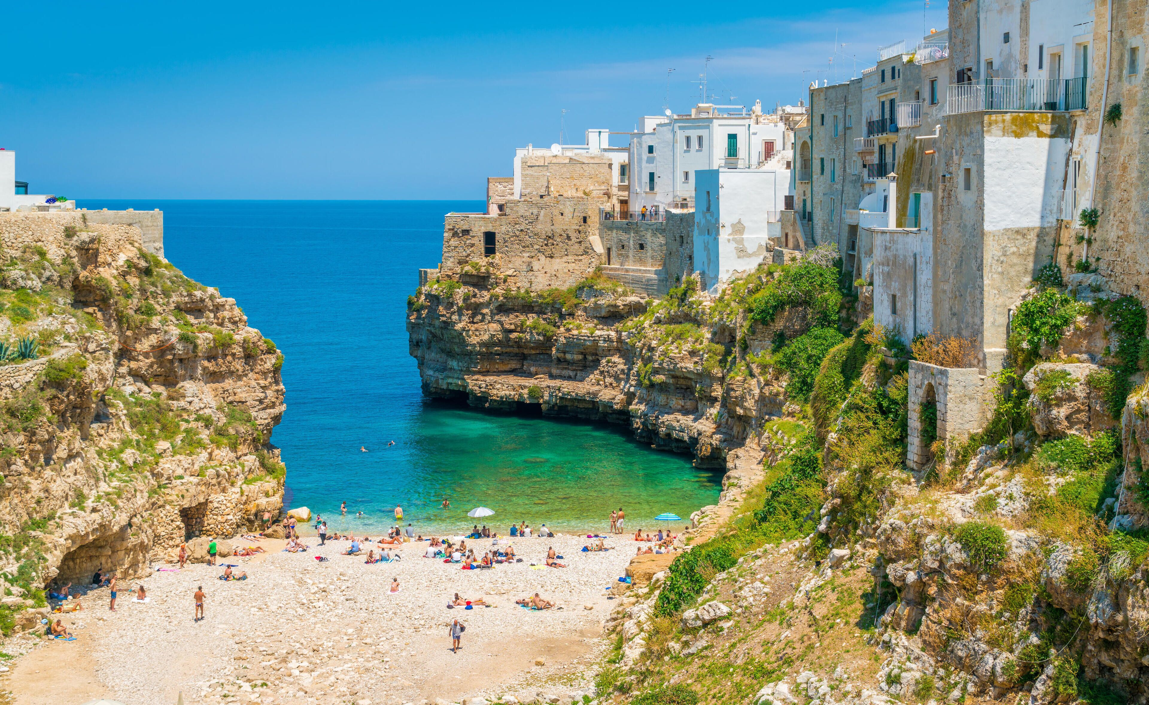 A coastal town with a rocky beach, clear blue sea, and historic buildings.