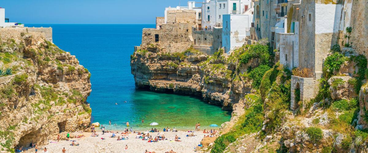 A coastal town with a rocky beach, clear blue sea, and historic buildings.