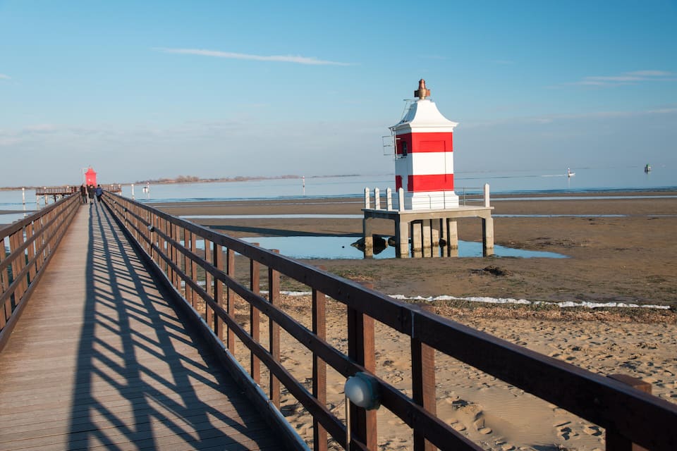 A wooden pier leading to a lighthouse on a sandy beach.