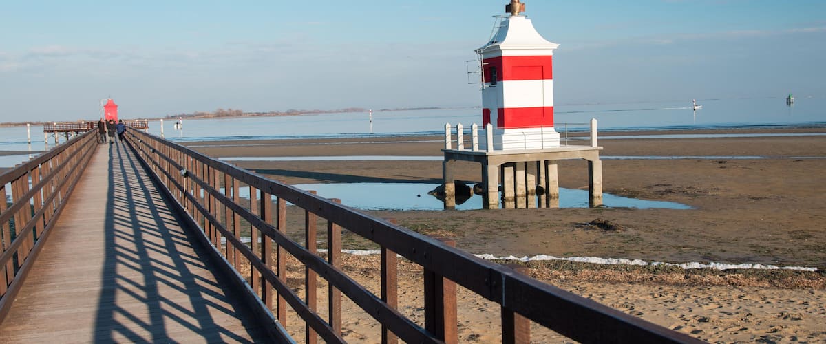 A wooden pier leading to a lighthouse on a sandy beach.