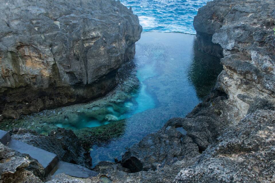 A narrow water channel between rocky cliffs with clear water reflecting the sky.
