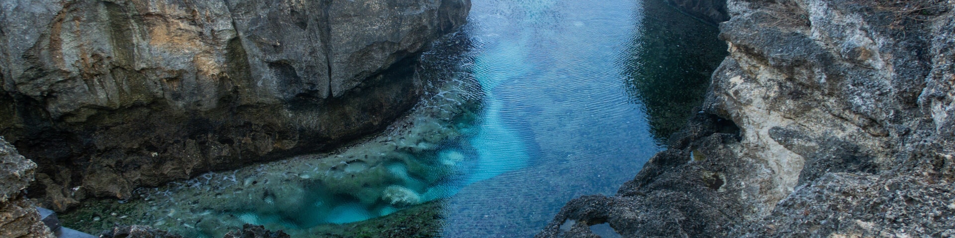 A narrow water channel between rocky cliffs with clear water reflecting the sky.