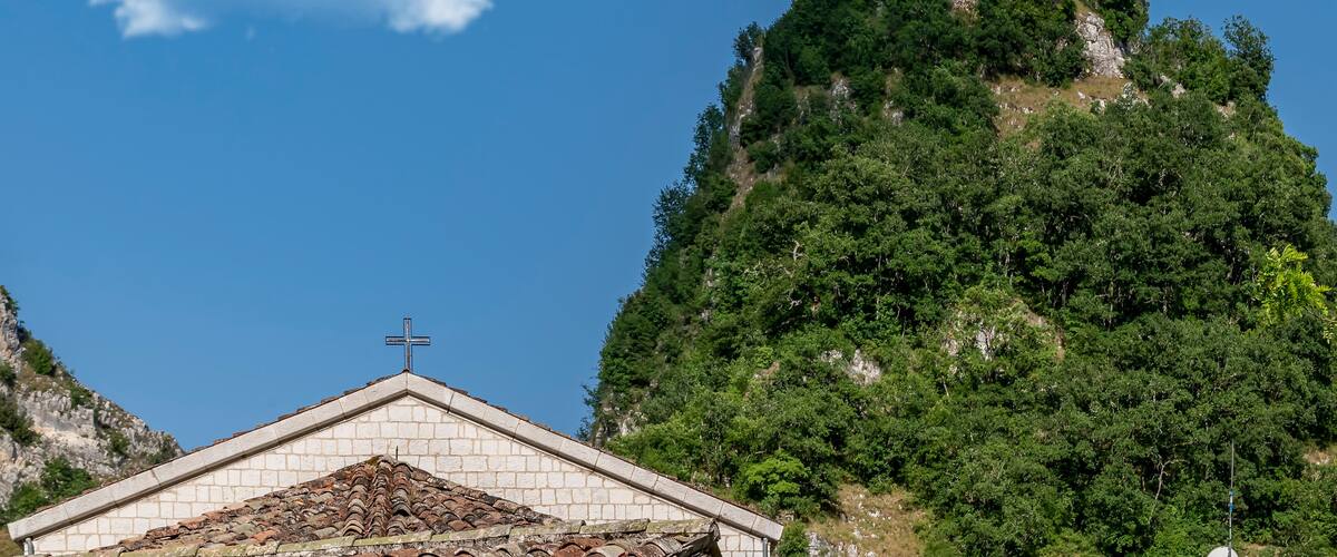 A church on a hilltop with a cross on the roof, surrounded by lush greenery.