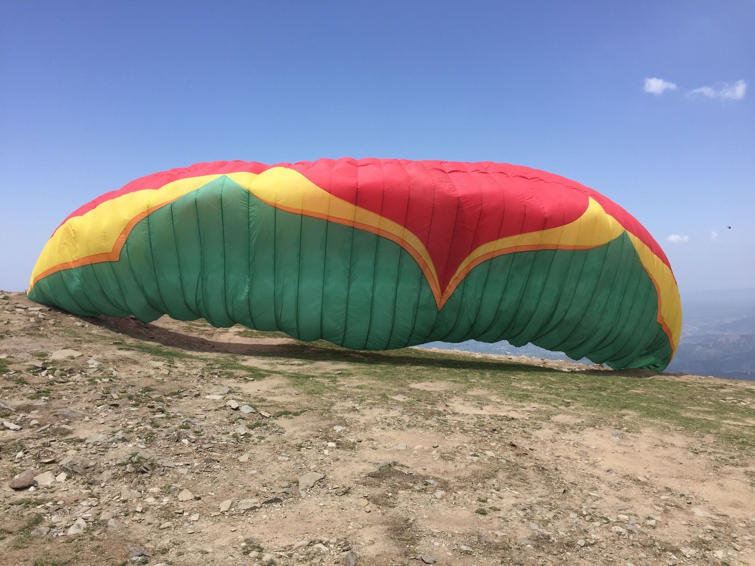 A large, colorful parasail on a rocky hillside.