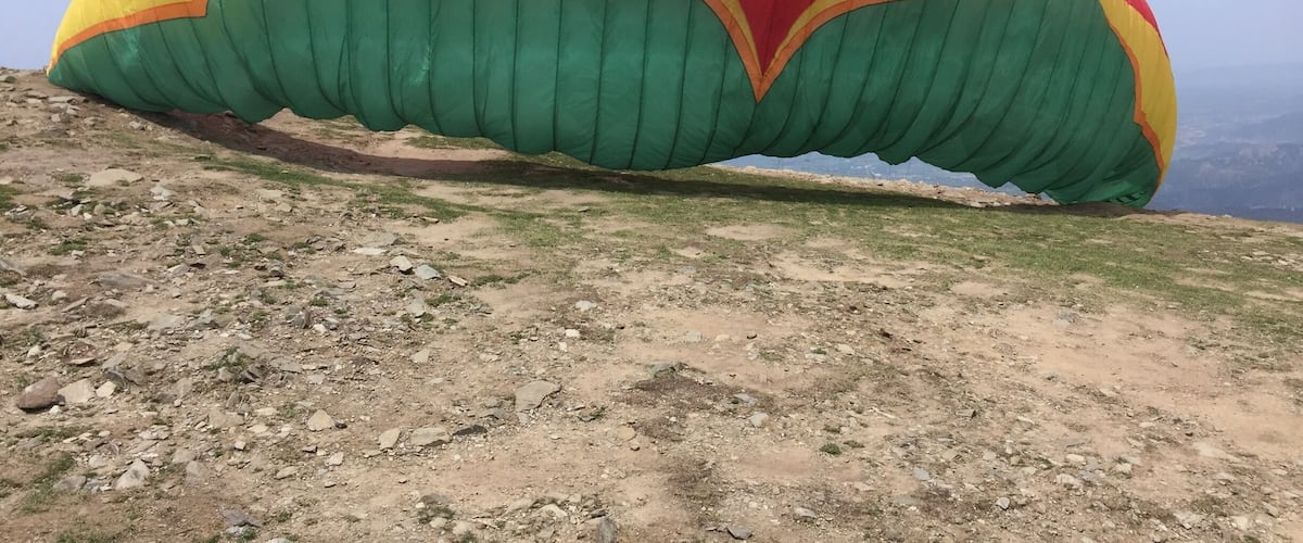 A large, colorful parasail on a rocky hillside.