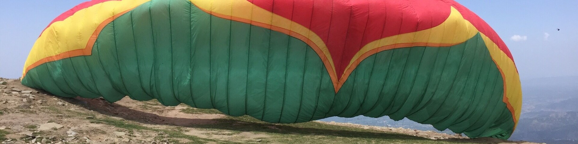 A large, colorful parasail on a rocky hillside.