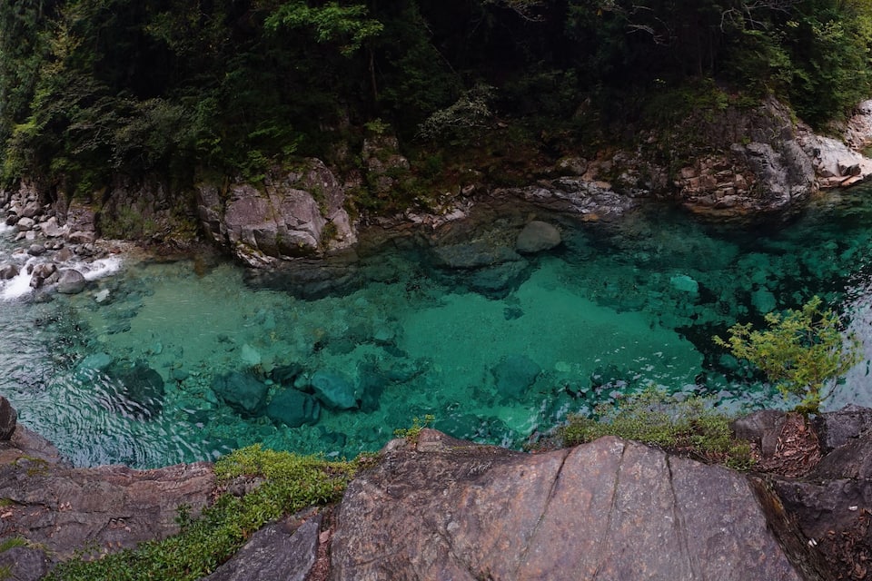 Un río turquesa y transparente rodeado de terreno rocoso y un bosque frondoso.