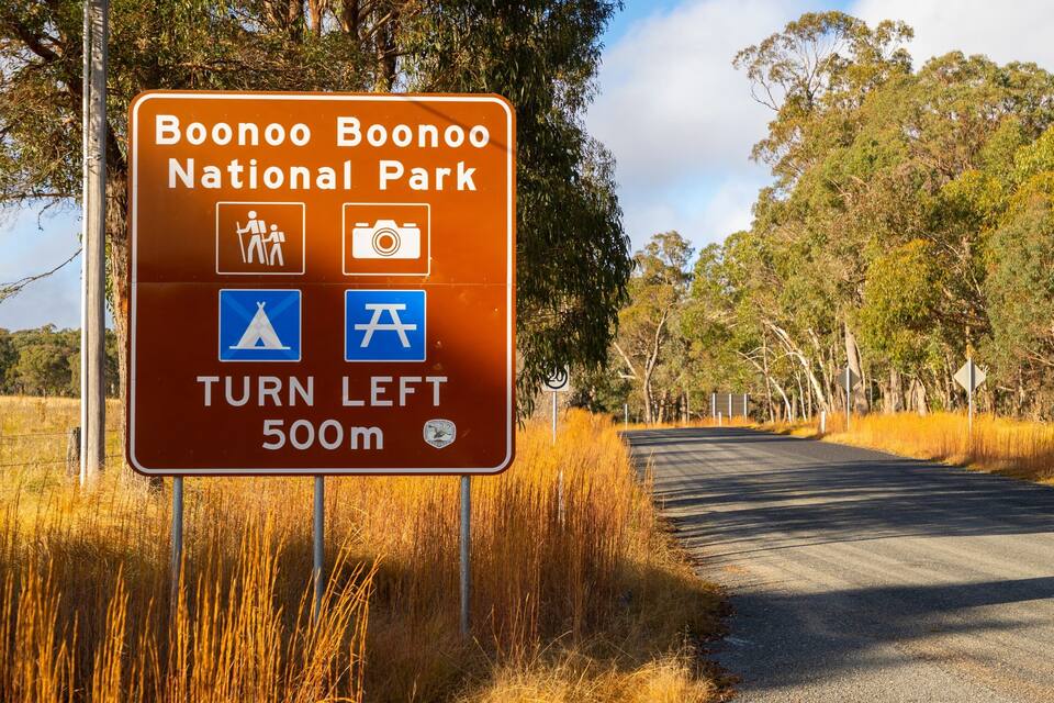 A sign for Boonoo Boonoo National Park with symbols for walking, photography, camping, and a tent. It instructs to turn left in 500m.