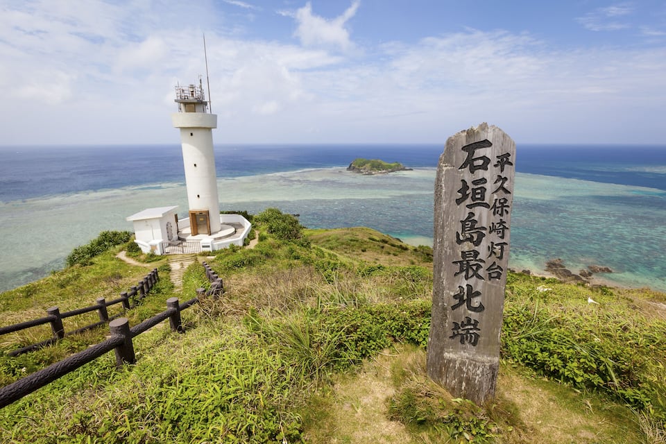 A lighthouse, a wooden sign, and a coastal landscape with clear waters and a small island.