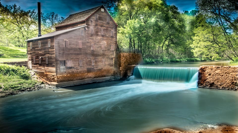A wooden mill by a river with a waterfall.
