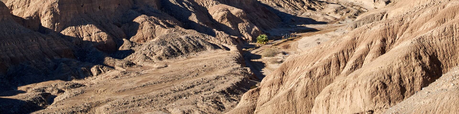 A rugged desert landscape with eroded hills and a clear sky.