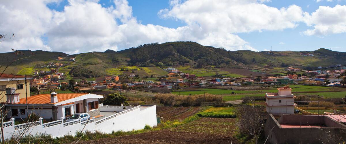 A rural landscape with rolling hills, scattered houses, and agricultural fields.
