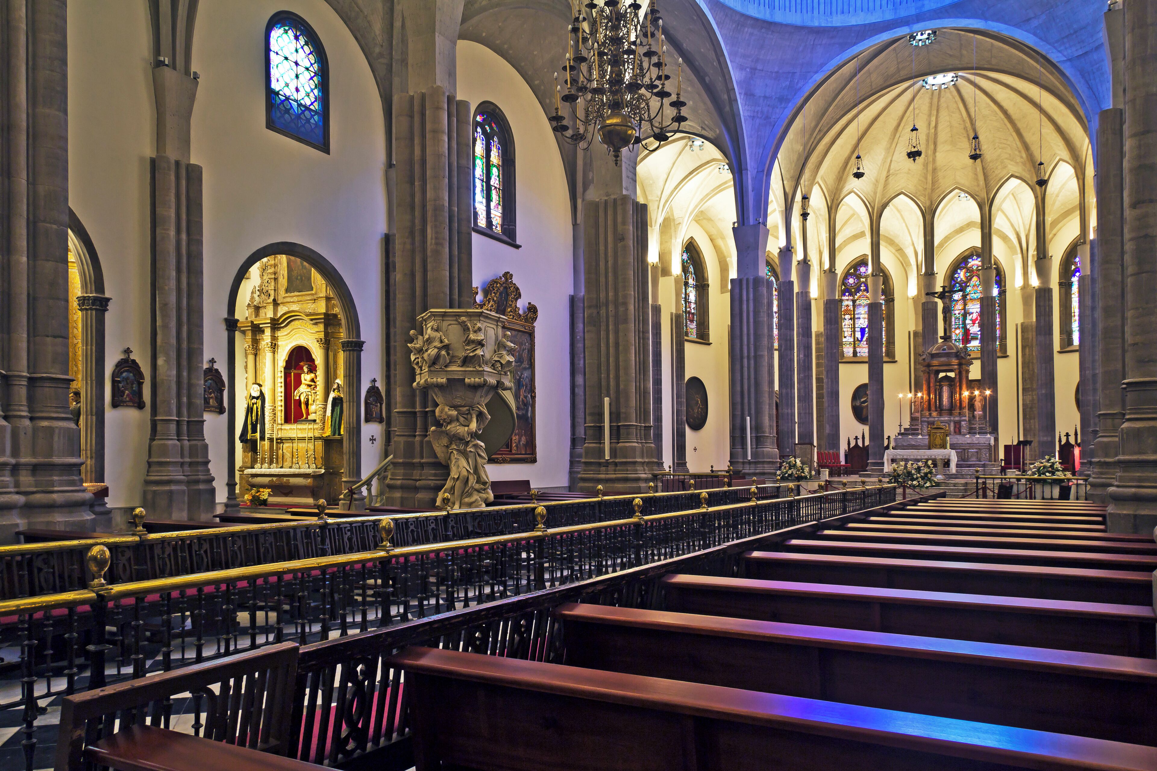 A church interior with arched ceilings, stained glass windows, and pews.