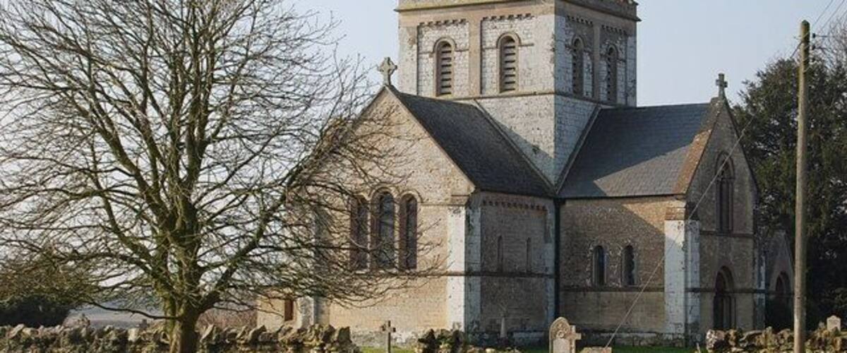 Een historische kerk met een opvallende toren en een stenen muur met grafstenen op de voorgrond.