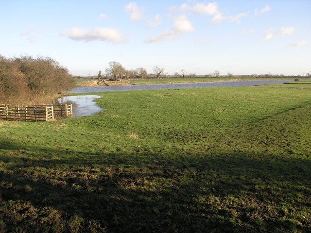 A grassy field with a wooden fence and a small water body.