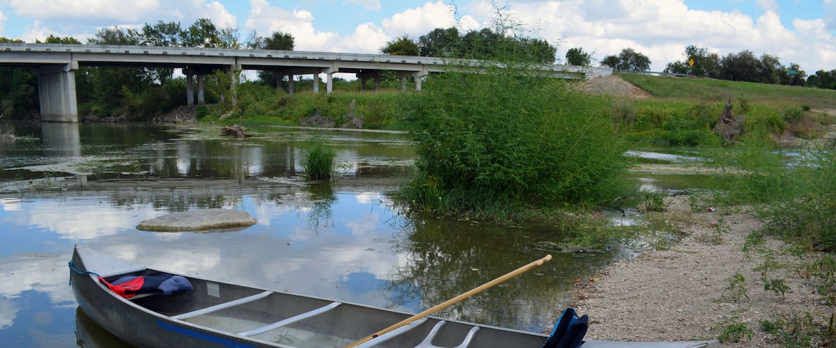 Canoe Beach/Two person canoe sitting on the bank of a river.