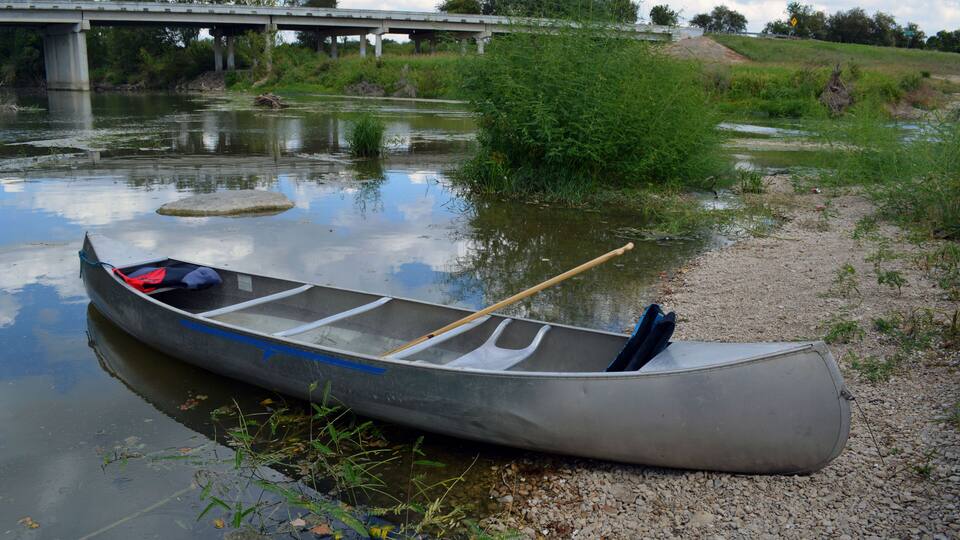 Canoe Beach/Two person canoe sitting on the bank of a river.