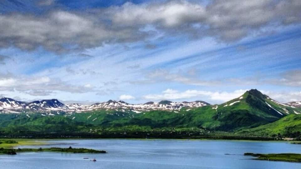 A lake surrounded by green hills and mountains under a partly cloudy sky.