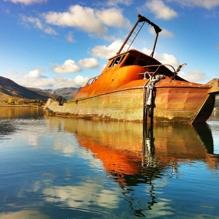 A rusted boat on calm water with mountains in the background.