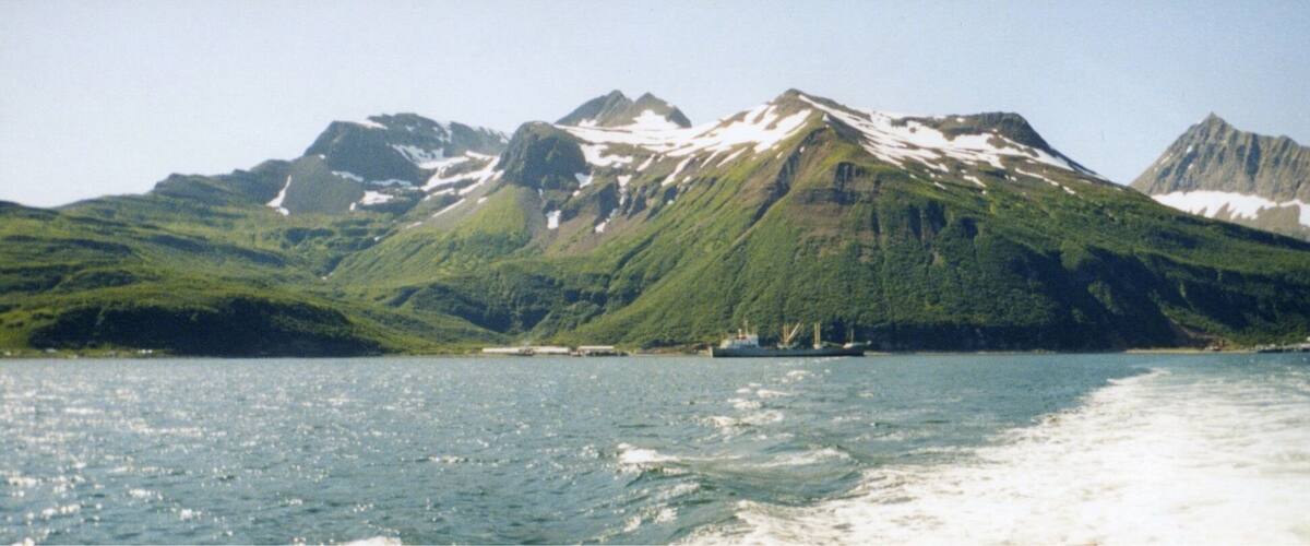 A boat on a calm lake with snow-capped mountains in the background.