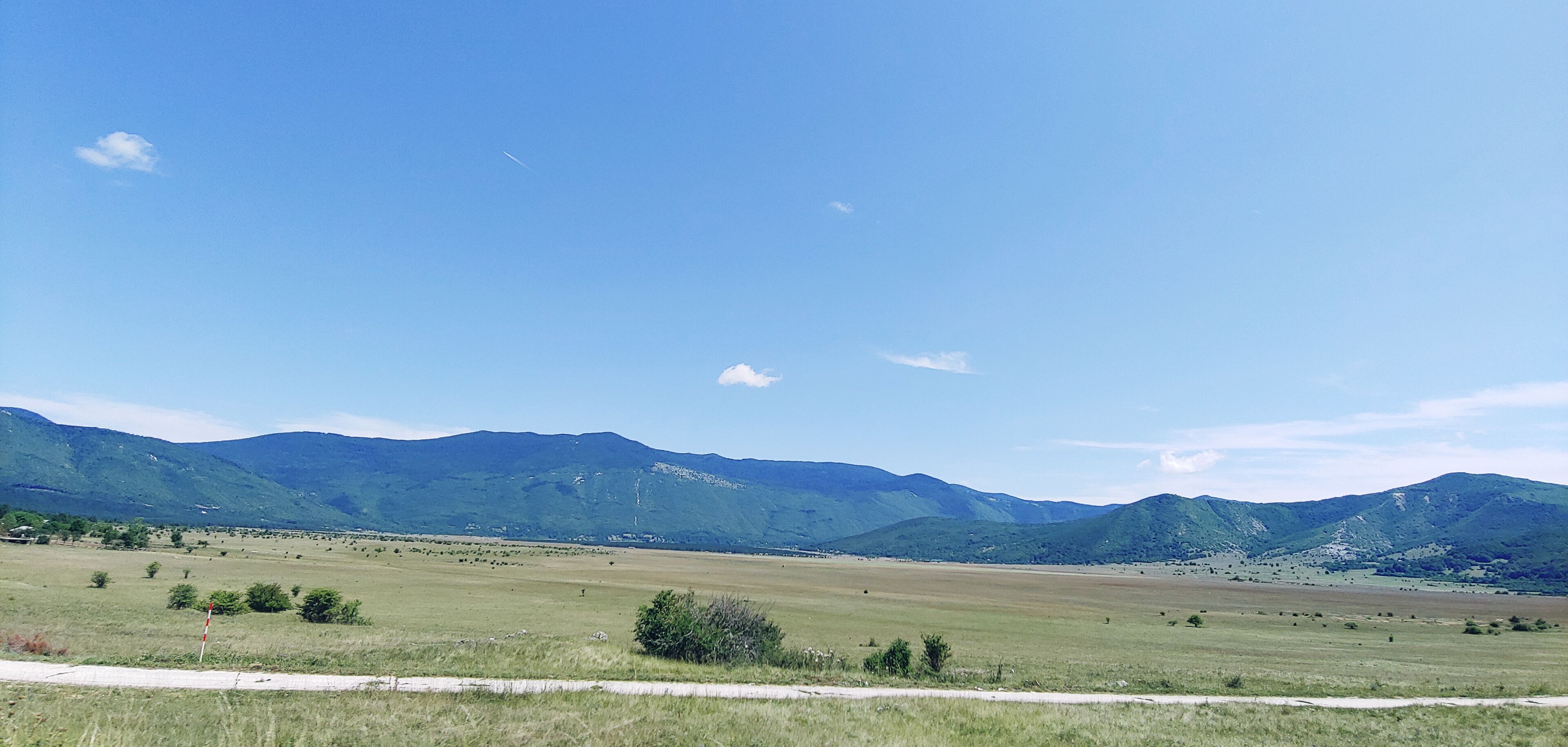 A vast open field with distant green mountains under a clear blue sky.