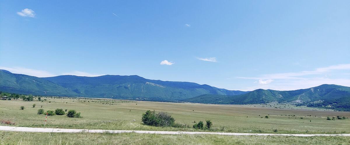 A vast open field with distant green mountains under a clear blue sky.