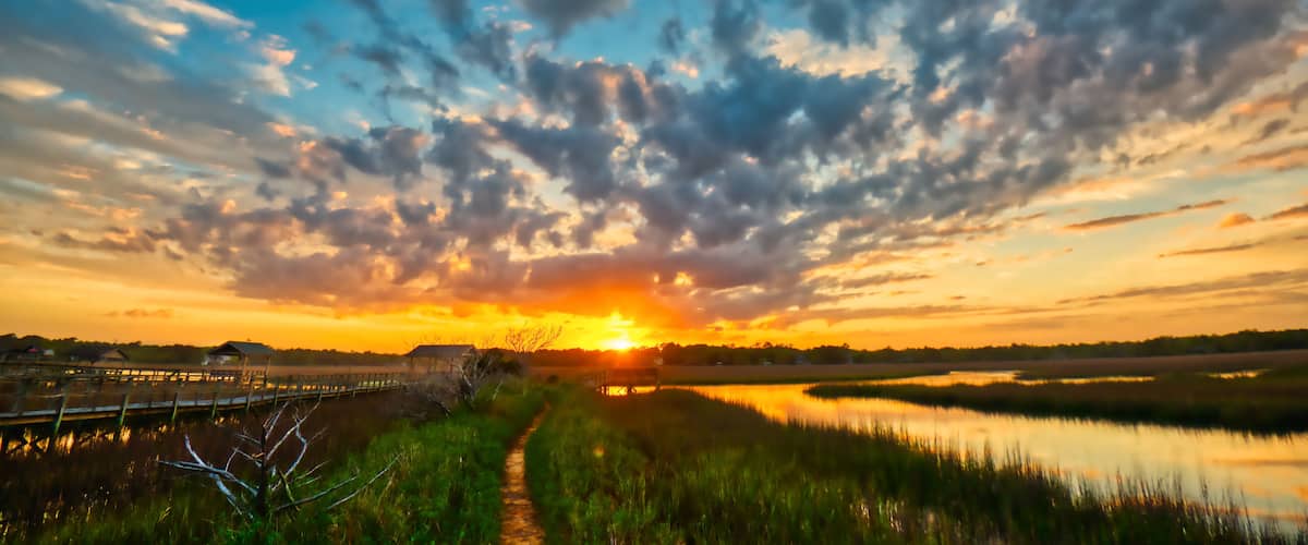 A sunset over a water body with a wooden walkway and grassy banks.