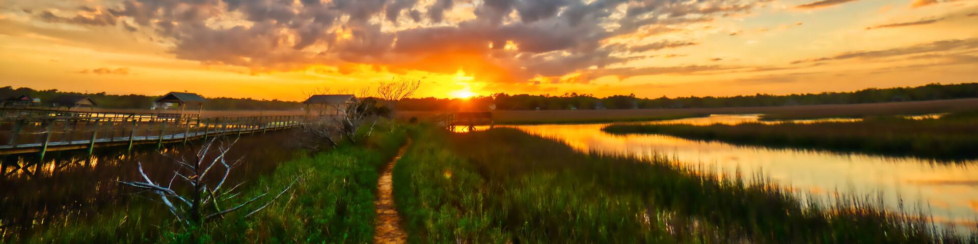 A sunset over a water body with a wooden walkway and grassy banks.