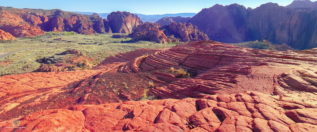 A vast desert landscape with prominent red rock formations and a clear blue sky.