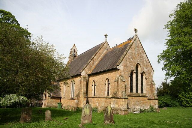 A stone church with a steep roof and multiple arched windows, surrounded by a grassy area with several headstones.
